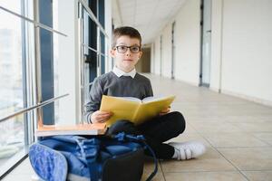 scolaro si siede su il pavimento di un' scuola corridoio e legge un' libro foto