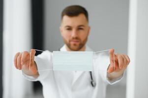 bello maschio medico nel medico uniforme mettere su protettivo maschera contro covid-19 virus. coronavirus protezione, assistenza sanitaria, medico attrezzatura foto