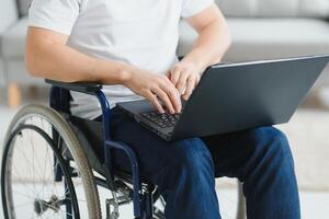 opera a casa. paralizzato maschio persona Tenere il computer portatile su ginocchia e conservazione Sorridi su viso mentre guardare a schermo foto