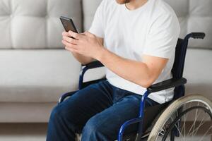 giovane contento imprenditore nel sedia a rotelle lettura Messaggio su inteligente Telefono a casa foto