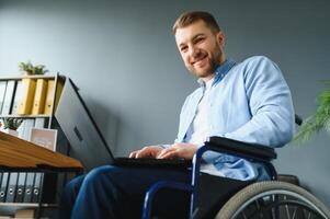 giovane contento imprenditore nel sedia a rotelle Lavorando su il computer portatile a casa. foto
