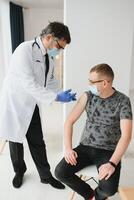 medicinale, vaccinazione e assistenza sanitaria concetto - medico indossare viso protettivo medico maschera per protezione a partire dal virus malattia con siringa fare iniezione di vaccino per maschio paziente. foto