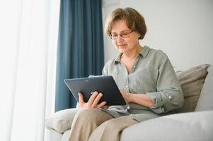 anziano donna utilizzando digitale tavoletta nel vivente camera a casa foto