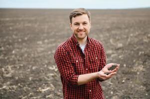 un' contadino nel stivali lavori con il suo tavoletta nel un' campo seminato nel primavera. un agronomo passeggiate il terra, valutare un' arato campo nel autunno. agricoltura. inteligente agricoltura tecnologie foto