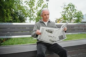 vecchio dai capelli grigi uomo riposo su il panchina nel estate parco foto