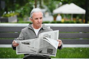 vecchio dai capelli grigi uomo riposo su il panchina nel estate parco foto