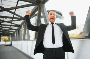 uomo d'affari sorridente e raccolta il suo cazzotto nel il aria, con ufficio edificio sfondo - attività commerciale successo, risultato, e vincere concetti foto