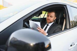 uomo di stile e stato. bello giovane uomo nel pieno completo da uomo sorridente mentre guida un' auto foto