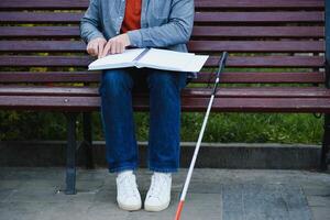 cieco uomo lettura braille prenotare, seduta su panchina nel estate parco, riposo foto