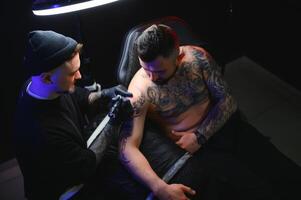 maschio tatuaggio artista Tenere un' tatuaggio pistola, mostrando un' processi di fabbricazione tatuaggi su un' maschio tatuato Modelli braccio foto