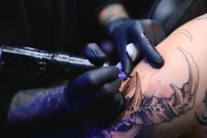 giovane professionale tatuaggio maestro introduce nero inchiostro in il pelle utilizzando un' ago a partire dal un' tatuaggio macchina. tatuaggio su mano foto