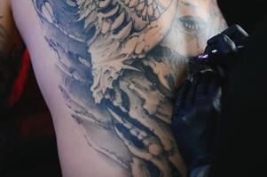 tatuaggio artista uomo con nero guanti disegna un' cavaliere tatuaggio su il ragazzi indietro nel il studio. tatuaggio dell'artista flusso di lavoro foto