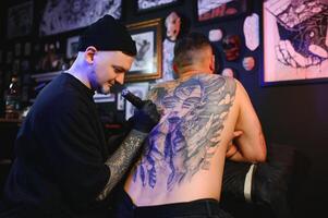 tatuaggio. uomo la creazione di un' immagine su il suo indietro di un' professionale tatuaggio artista foto