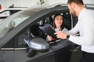 soddisfatto contento caucasico femmina cliente cliente donna seduta a il ruota di nuovo auto mentre maschio negozio assistente porzione sua scegliere esso foto