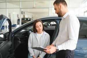 soddisfatto contento caucasico femmina cliente cliente donna seduta a il ruota di nuovo auto mentre maschio negozio assistente porzione sua scegliere esso foto