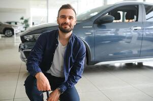 sì, quello è mio nuovo auto cliente nel auto concessionaria. giovane uomo inginocchiato giù con chiavi nel mano foto