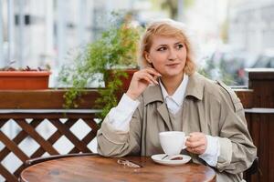 moda ritratto di giovane donna ubicazione a il tavolo con tazza di caffè, tè nel strada bar. foto