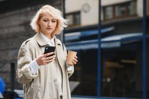 bellissimo elegante donna avendo bene moda Abiti a piedi su strada e potabile alcuni caffè nel tazza porta via con bene estate umore vicino strada bar. foto