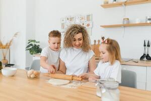 contento giovane madre con carino poco bambino in età prescolare bambini avere divertimento fabbricazione Impasto cottura al forno torta o Pasticcino nel moderno cucina insieme, felicissimo madre insegnare piccolo bambini fare forno cucinando a casa foto