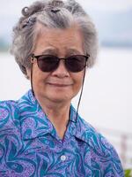 ritratto di anziano donna corto bianca capelli in piedi indossare occhiali da sole e sorridente a lato il fiume. concetto di vecchio persone e viaggio foto