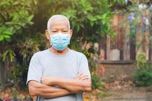 un' anziano uomo indossare un' viso maschera e guardare a il telecamera mentre in piedi nel un' giardino. maschera per protezione virus, covid19, coronavirus, batteri, polvere. concetto di anziano persone e assistenza sanitaria foto