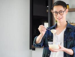 un' giovane uomo indossare casuale capi di abbigliamento uso un' frusta miscelazione ingredienti nel un' ciotola mentre in piedi nel il cucina. cucina utensili e cucinando concetto foto