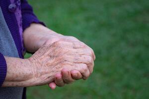 avvicinamento di rugosa mani anziano donna Iscritto insieme mentre in piedi all'aperto. concetto di anziano persone e assistenza sanitaria foto