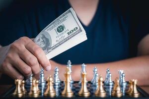 avvicinamento foto di dollari moneta nel mano un' uomo con primo piano sfocatura scacchi gioco. attività commerciale gioco competitivo strategia. concetto di strategia per attività commerciale