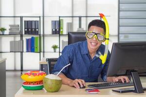 giovane uomo indossare un' immersione maschera giallo, sorridente e seduta su un' sedia Lavorando nel il suo ufficio. lui è un' sognare di il mare perché il vacanza In arrivo presto. vacanza concetto foto