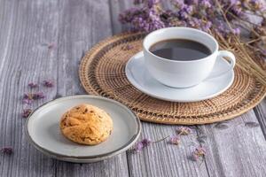 avvicinamento di un' biscotto su un' piatto con un' bianca caffè tazza e fiore sfocato sfondo. spazio per testo foto