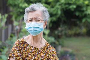 ritratto di un' anziano indossare un' viso maschera e guardare a il telecamera mentre in piedi nel un' giardino. maschera per protezione di covid19, virus, coronavirus, eccetera. concetto di anziano persone e assistenza sanitaria foto