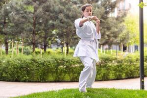 giovane attivo ragazza indossare nel bianca chimono con bianca cintura l'esecuzione marziale arti calcio abilità. sportivo karatè donna miglioramento combattimento tecnica su Cinese ponte. concetto di sport. foto