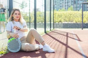 contento femmina pagaia tennis giocatore durante pratica su all'aperto Tribunale guardare a telecamera. copia spazio. foto