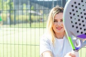 contento femmina pagaia tennis giocatore durante pratica su all'aperto Tribunale guardare a telecamera. copia spazio. foto