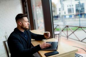 giovane libero professionista o uomo d'affari lavori su giro superiore e bevande caffè nel un' bar. grande panoramico finestre nel davanti. avvicinamento. foto