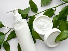 vicino su di bianca lozione bottiglia e mano crema contenitore con verde le foglie su bianca sfondo. cura della pelle e naturale bellezza concetto. per assistenza sanitaria, benessere, e biologico Prodotto manifesto. foto