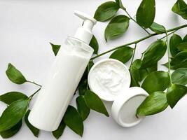 vicino su di bianca lozione bottiglia e mano crema contenitore con verde le foglie su bianca sfondo. cura della pelle e naturale bellezza concetto. per assistenza sanitaria, benessere, e biologico Prodotto manifesto. foto