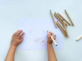 piccolo bambino disegna con colorato matite su carta su bianca tavolo. foto