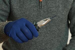 un' dell'uomo mano nel un' blu protettivo guanto detiene un' nero chiodo con pinze. foto