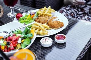 delizioso piatto di fritte pollo, francese patatine fritte, insalata e un' bicchiere di vino foto