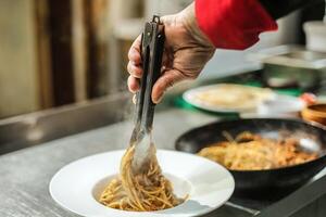 persona utilizzando pinza per agitare tagliatelle su un' piatto foto