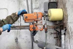 lavoratore utilizzando un elettrico trapano per rendere un' buco nel un' calcestruzzo parete, avvicinamento foto