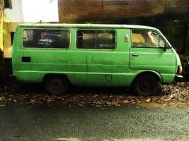 surakarta città, centrale Giava, Indonesia, aprile 15, 2024 Vintage ▾ immagine di un' verde vecchio e classico minivan auto parcheggio su il lato di il strada nel il mattina. arrugginito automobile abbandonato su il strada foto