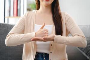 un' giovane sordo donna è seduta su un' divano e fabbricazione un' cartello linguaggio per comunicare. foto