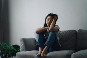 infelice solitario depresso donna è seduta su il divano e Tenere sua testa. foto
