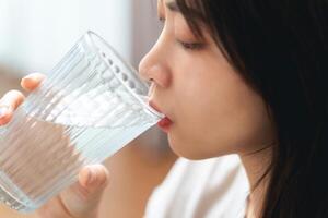 vicino su tiro di un' donna potabile acqua a partire dal un' bicchiere. sano, cibo e bevanda concetto. foto