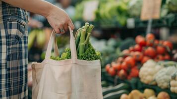 un' avvicinamento tiro di un' di persona mano Tenere un' riutilizzabile shopping Borsa con verdure nel il sfondo a un' Locale agricoltori mercato. foto