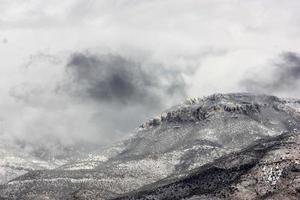 minacciose nuvole temporalesche e neve che soffia su un vasto paesaggio montano foto