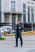 elegante maschio nel formale Abiti. modello uomo indossa completo da uomo e grigio cappotto. moderno edificio con bene architettura su il sfondo. foto