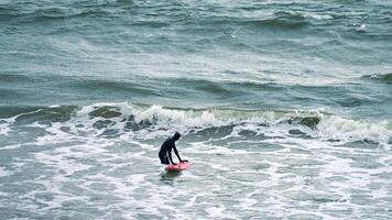surfista maschio in costume da bagno nelle onde del mare con tavola da surf rossa foto